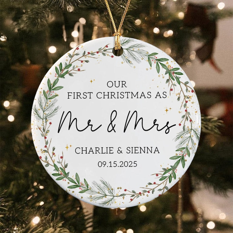 A round white ceramic ornament featuring a green pine and berry wreath design. The text reads: OUR FIRST CHRISTMAS AS Mr & Mrs CHARLIE & SIENNA 09.15.2025.