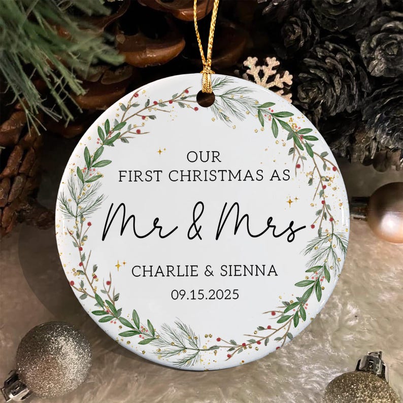 A round white ceramic ornament featuring a green pine and berry wreath design. The text reads: OUR FIRST CHRISTMAS AS Mr & Mrs, CHARLIE & SIENNA, 09.15.2025.