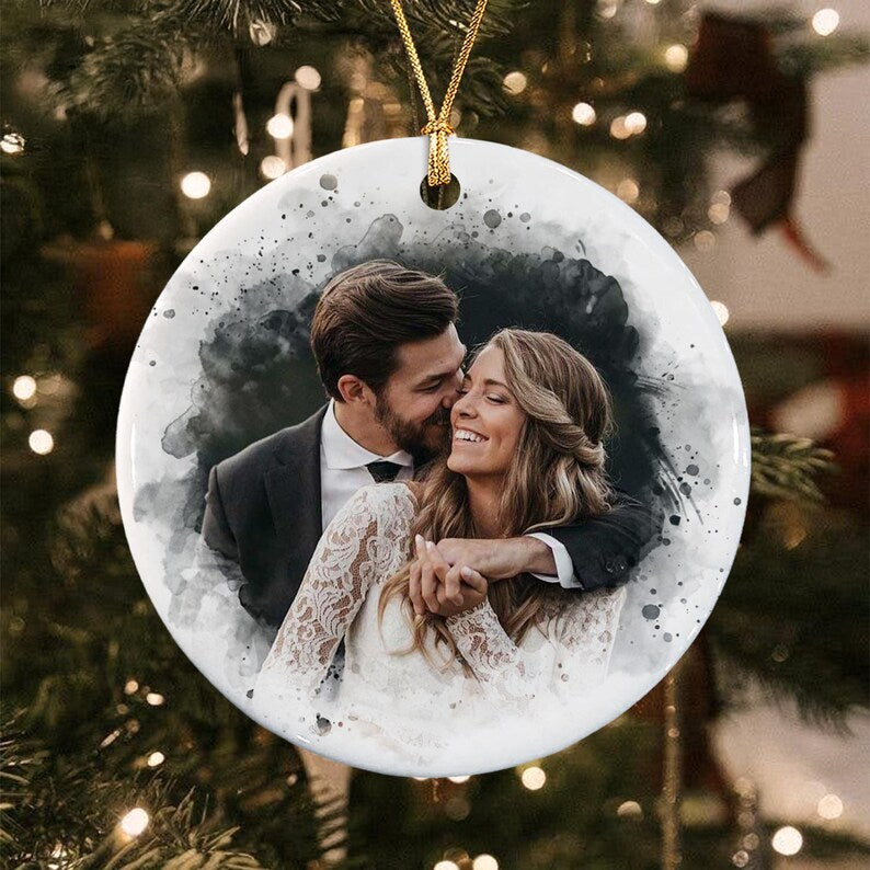 A round white ceramic ornament featuring a watercolor-style portrait of a couple embracing. The person on the left wears a dark suit and the person on the right wears a white lace long-sleeve dress.