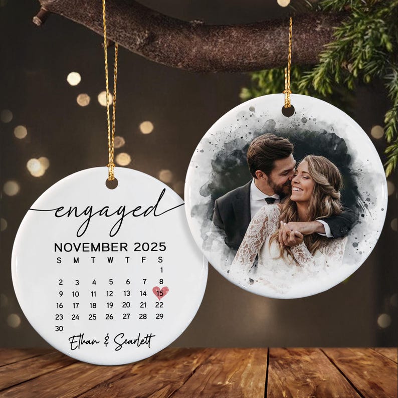 Two round white ceramic ornaments hanging by gold strings. One ornament features the text engaged, November 2025, a calendar with a heart on the 15th, and the names Ethan and Scarlett.