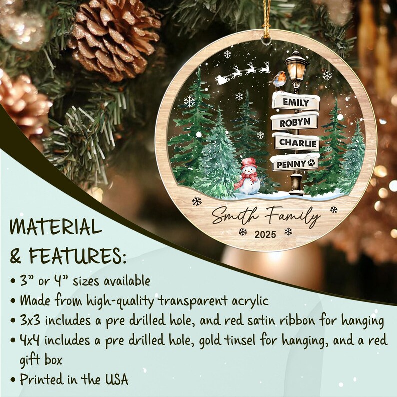 A round transparent acrylic Christmas ornament featuring a winter scene with green pine trees, a snowman, a street lamp with signs reading EMILY, ROBYN, CHARLIE, and PENNY, a flying sleigh, and the text Smith Family 2025.