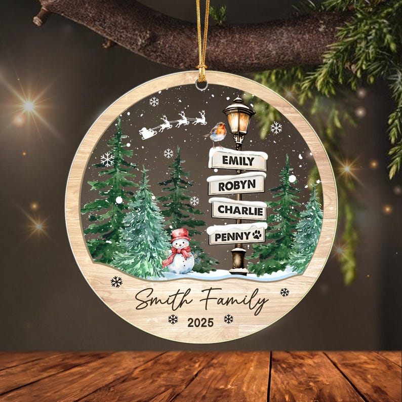 A round, wood-look Christmas ornament featuring a winter scene with green pine trees, a snowman, a street lamp with signs reading Emily, Robyn, Charlie, and Penny, a robin, a flying sleigh, and the text Smith Family 2025.