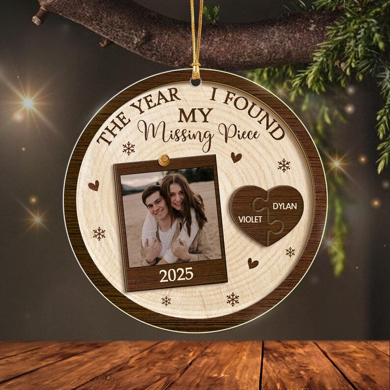 A round wooden ornament featuring the text THE YEAR I FOUND MY Missing Piece and 2025. It displays a square photo of two people and a heart-shaped puzzle piece ornament with the names VIOLET and DYLAN engraved on it.