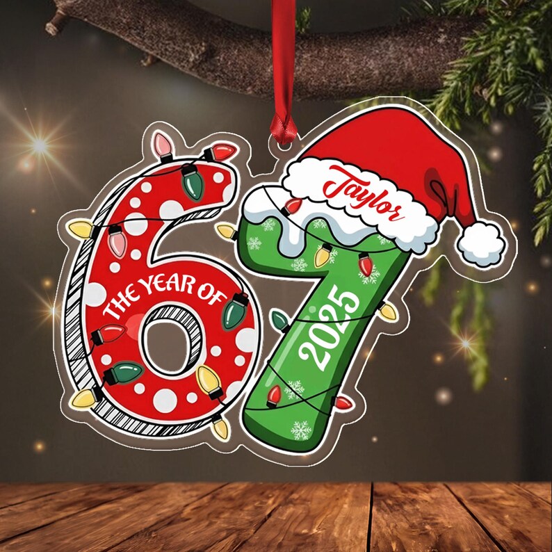 A decorative ornament shaped like the number 67, featuring a red polka-dot 6 and a green 7. The 6 includes the text THE YEAR OF, while the 7 displays the year 2025 and the name Taylor. It is adorned with colorful Christmas lights.