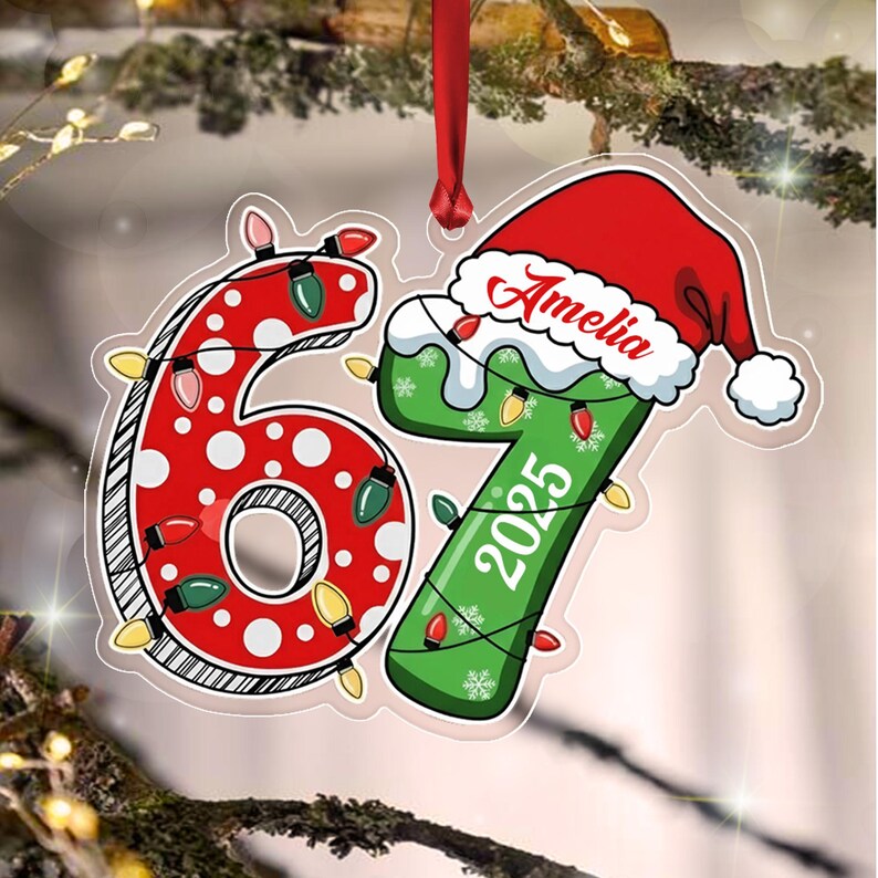A flat, die-cut Christmas ornament shaped like the number 67. The 6 is red with white polka dots, and the 7 is green with the year 2025 and a red Santa hat featuring the name Amelia.