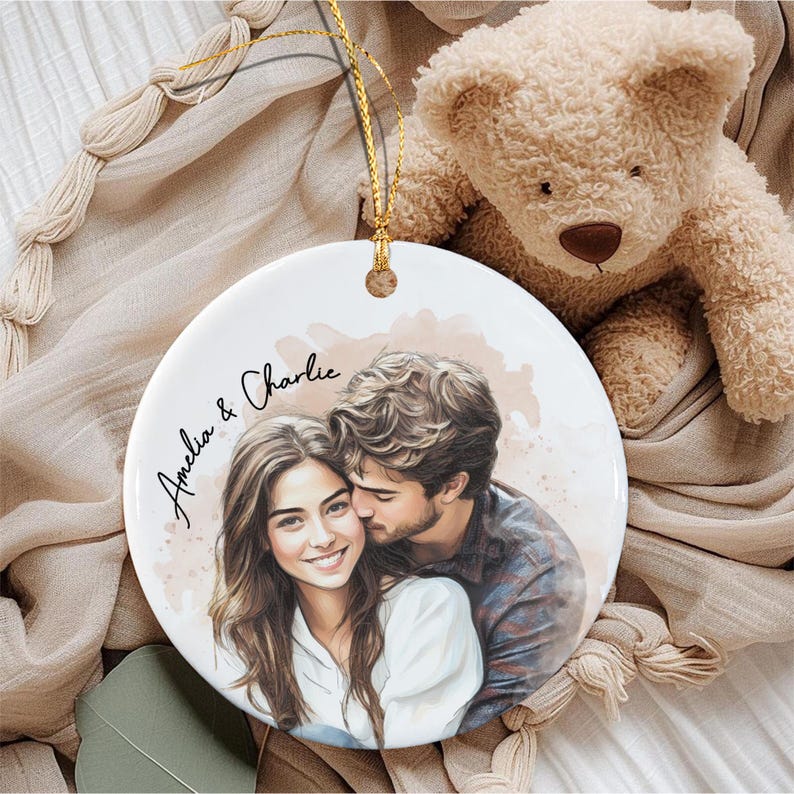 A round white ceramic ornament featuring a watercolor-style illustration of a couple embracing. The text "Amelia & Charlie" is printed in black script on the left side.