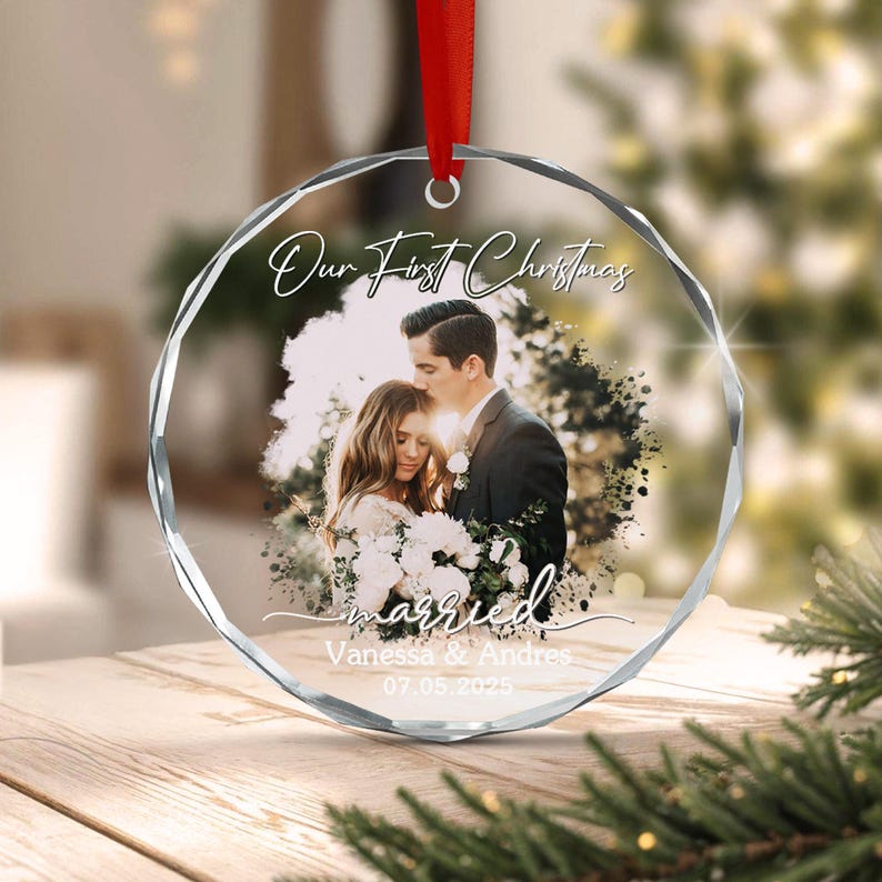 A round, faceted glass Christmas ornament featuring a printed photograph of a couple embracing. The text "Our First Christmas" appears at the top, with "married" and the names "Vanessa & Andres" and date "07.05.2025" below.