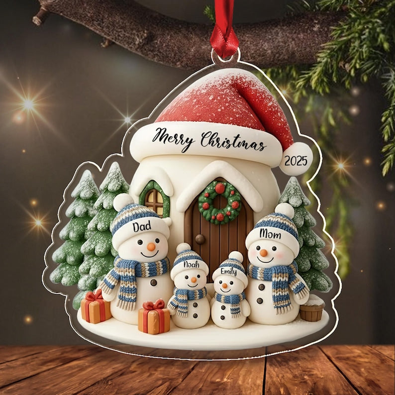 A clear acrylic Christmas ornament featuring a house with a red Santa hat roof, snow-covered pine trees, and four snowmen figures labeled Dad, Mom, Noah, and Emily. The ornament displays the text Merry Christmas and the year 2025.