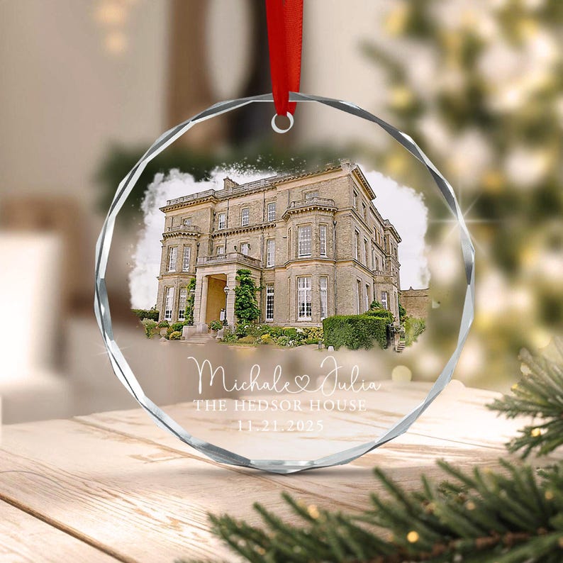 A circular faceted glass ornament featuring a printed illustration of a large stone mansion. The text reads Michale & Julia, THE HEDSOR HOUSE, and 11.21.2025. A red ribbon is attached to the top for hanging this decorative piece.