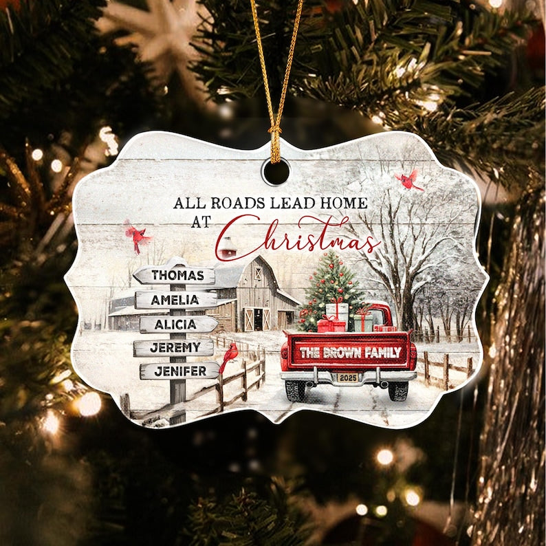 A decorative ornament featuring a winter scene with a red pickup truck, a barn, and a signpost with the names Thomas, Amelia, Alicia, Jeremy, and Jenifer. The text reads All Roads Lead Home At Christmas and The Brown Family 2025.