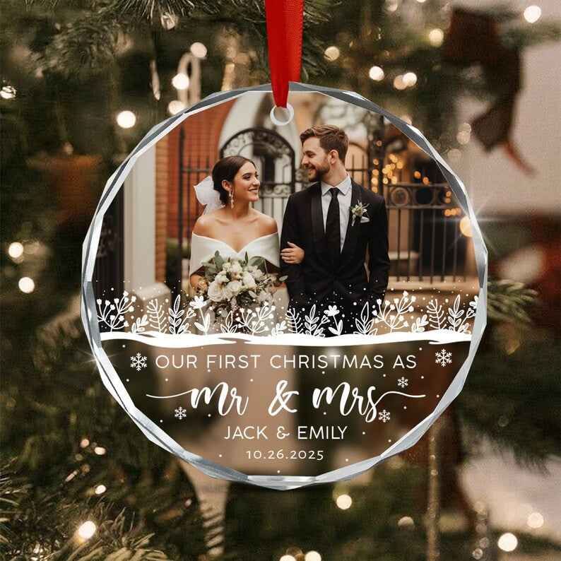 A round, faceted glass Christmas ornament featuring a photograph of a couple in wedding attire. The text reads: OUR FIRST CHRISTMAS AS MR & MRS JACK & EMILY 10.26.2025.