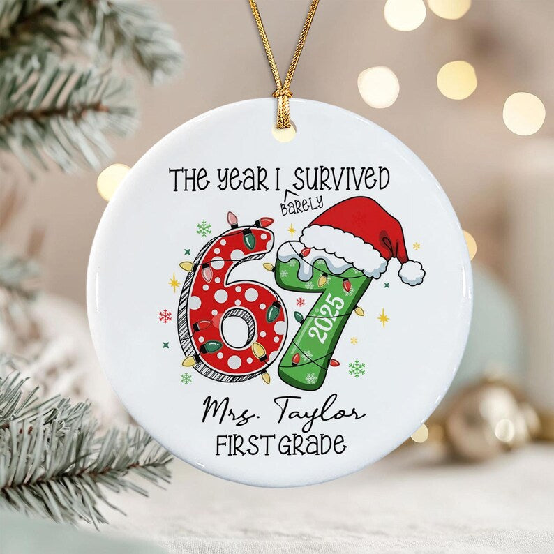 A round white ceramic ornament with a gold string. The text reads The year I barely survived 67. The number 6 is red with white dots and Christmas lights, and the 7 is green with a Santa hat and the year 2025. Below is Mrs.