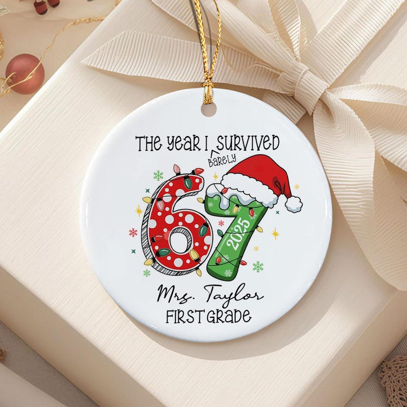 A round white ceramic ornament featuring the text "THE YEAR I BARELY SURVIVED" above a large red polka-dot number 6 and a green number 7 wearing a Santa hat with "2025" printed on it. Below are the words "Mrs. Taylor FIRST GRADE".