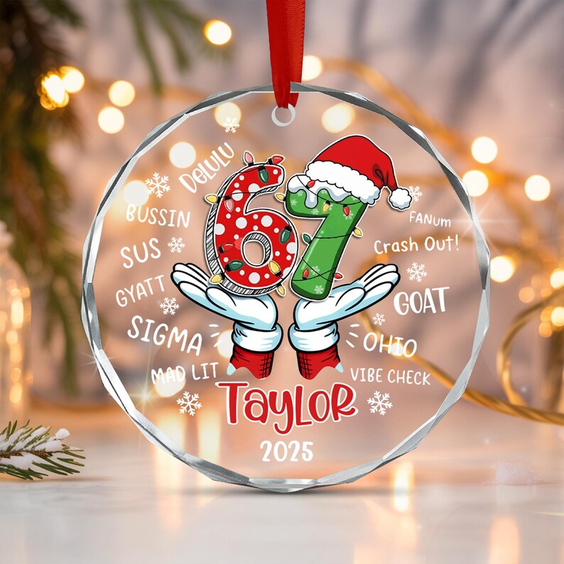 A circular clear acrylic Christmas ornament featuring the number 67, with the 6 in red with white polka dots and the 7 in green wearing a Santa hat. The text includes Taylor, 2025, and slang terms like Delulu, Bussin, and Goat.