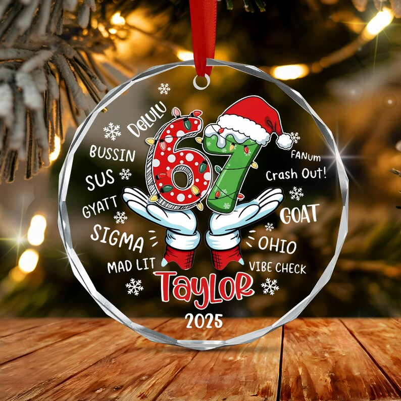 A round, clear acrylic Christmas ornament featuring the number 67 in red and green with a Santa hat.