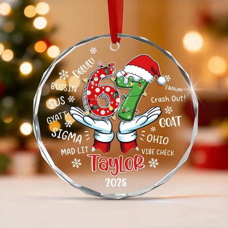 A circular clear acrylic Christmas ornament featuring the number 67 in red and green with a Santa hat, cartoon gloved hands, and the text Delulu, Bussin, Sus, Gyatt, Sigma, Mad Lit, Taylor, 2025, Fanum, Crash Out, Goat, Ohio.