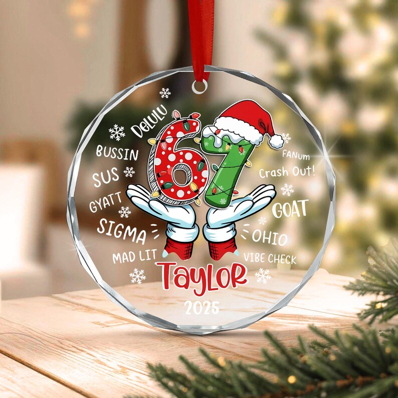A round, clear acrylic Christmas ornament featuring the number 67 in red and green with a Santa hat.