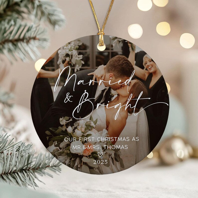 A round ceramic Christmas ornament featuring a photograph of a couple kissing at their wedding. The text reads Married & Bright, OUR FIRST CHRISTMAS AS MR. & MRS. THOMAS, and 2025. It hangs from a gold cord.