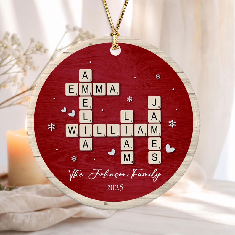 A round, red, wood-grain textured ornament featuring a crossword-style arrangement of letter tiles spelling the names Emma, Amelia, William, Liam, and James.