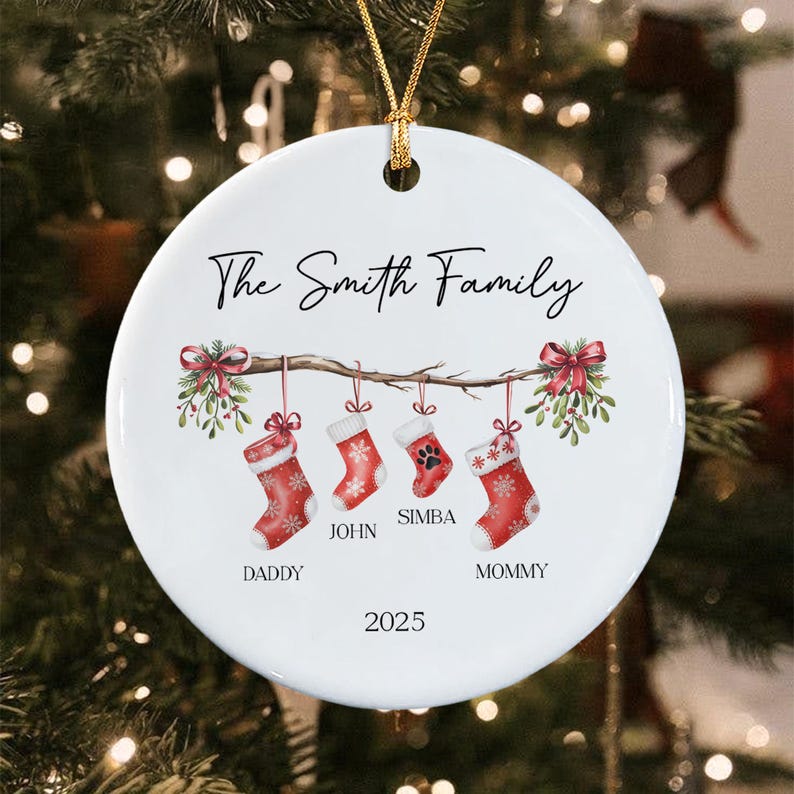 A round white ceramic Christmas ornament featuring a branch with four hanging red stockings with white snowflake patterns. The text reads The Smith Family, Daddy, John, Simba, Mommy, and 2025. A gold string is attached to the top.