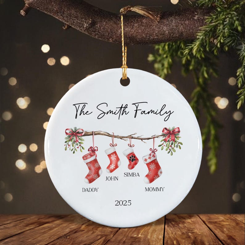 A round white ceramic ornament featuring the text The Smith Family at the top and 2025 at the bottom. The center displays a branch with red bows and four hanging red Christmas stockings labeled Daddy, John, Simba, and Mommy.