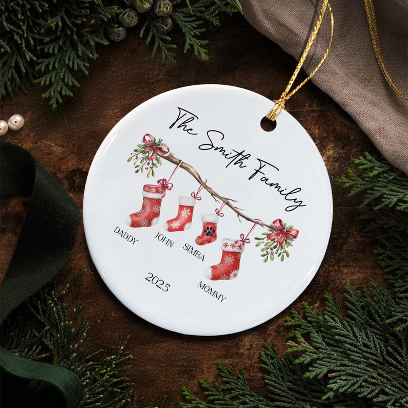 A round white ceramic ornament featuring a printed illustration of a tree branch with four red Christmas stockings hanging from it. The text reads The Smith Family, Daddy, John, Simba, Mommy, and 2025.