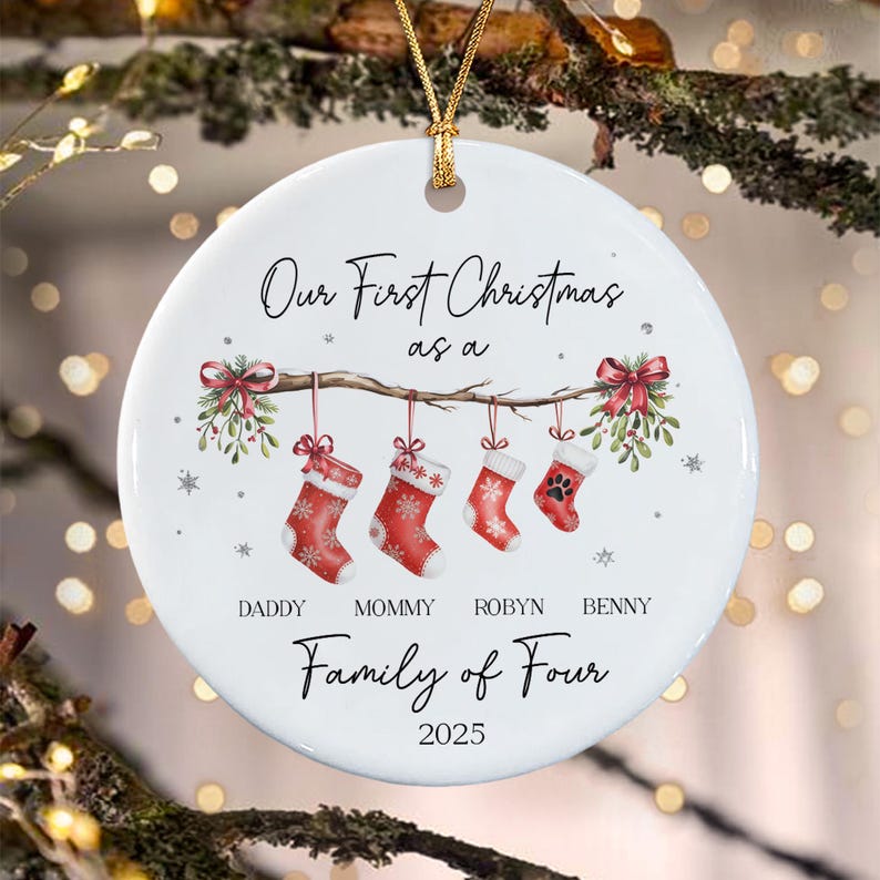 A round white ceramic Christmas ornament featuring a branch with four hanging red stockings, mistletoe, and the text Our First Christmas as a Family of Four, with names Daddy, Mommy, Robyn, Benny, and the year 2025 printed below.