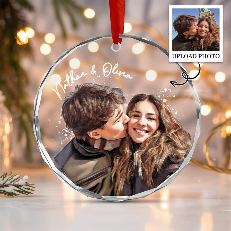 A circular, faceted clear acrylic ornament featuring a custom printed illustration of a couple. The text "Nathan & Olina" is printed in white script above the couple. A red ribbon is attached to the top for hanging.