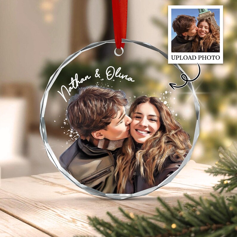 A circular clear acrylic ornament with faceted edges, featuring a printed illustration of a couple embracing. The text Nathan & Olina is printed in white script above the couple. A red ribbon is attached to the top for hanging.