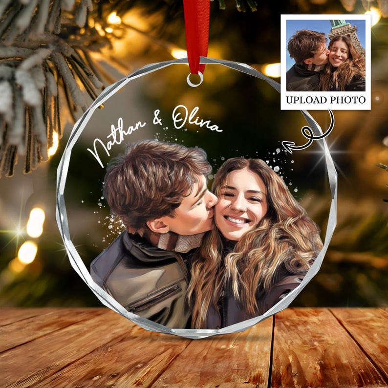 A circular, faceted glass ornament featuring a custom illustration of a couple with the text Nathan & Olivia. The ornament hangs from a red ribbon and displays a digital rendering of a couple, with a small inset photo above.