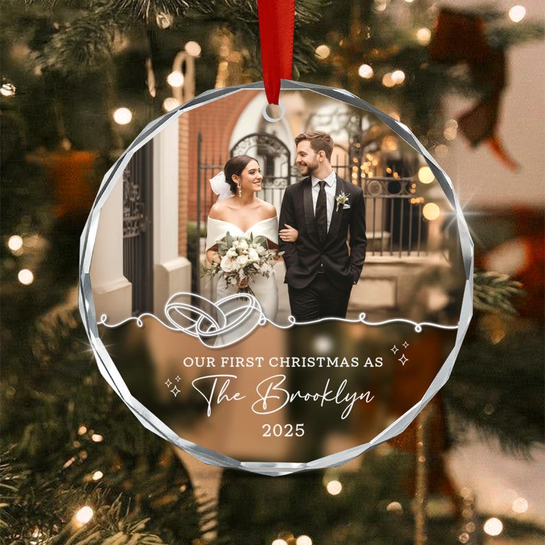 A round, faceted glass Christmas ornament featuring a printed photograph of a couple in wedding attire.