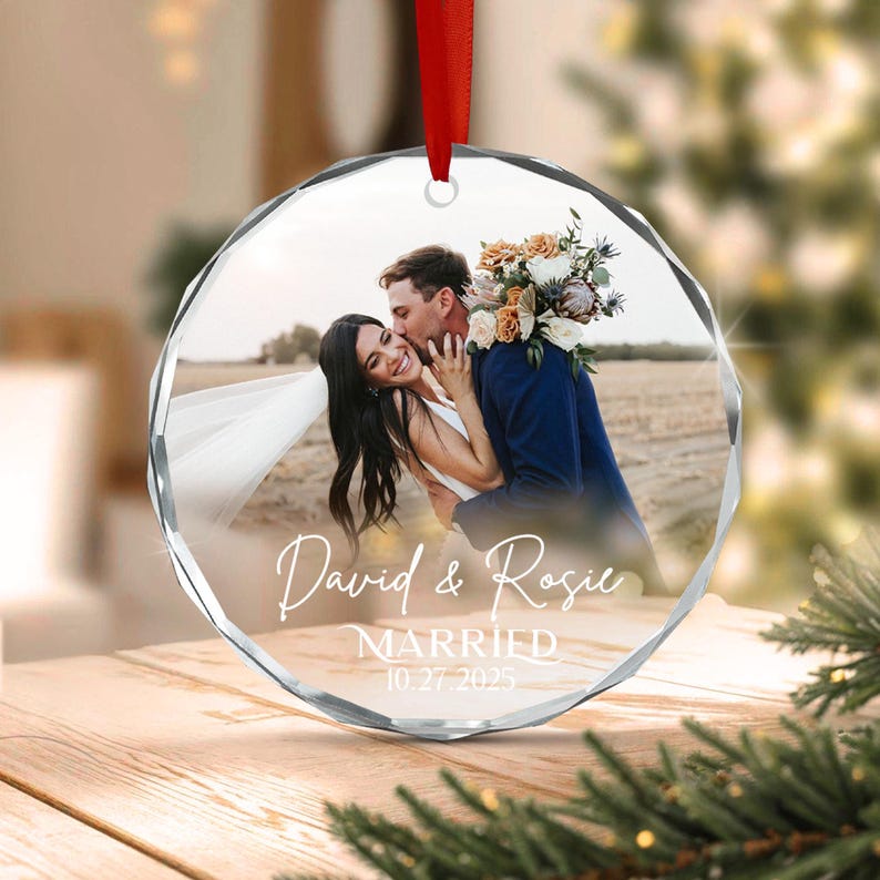 A circular, faceted glass ornament featuring a printed photograph of a couple embracing outdoors. The text reads David & Rosie MARRIED 10.27.2025.