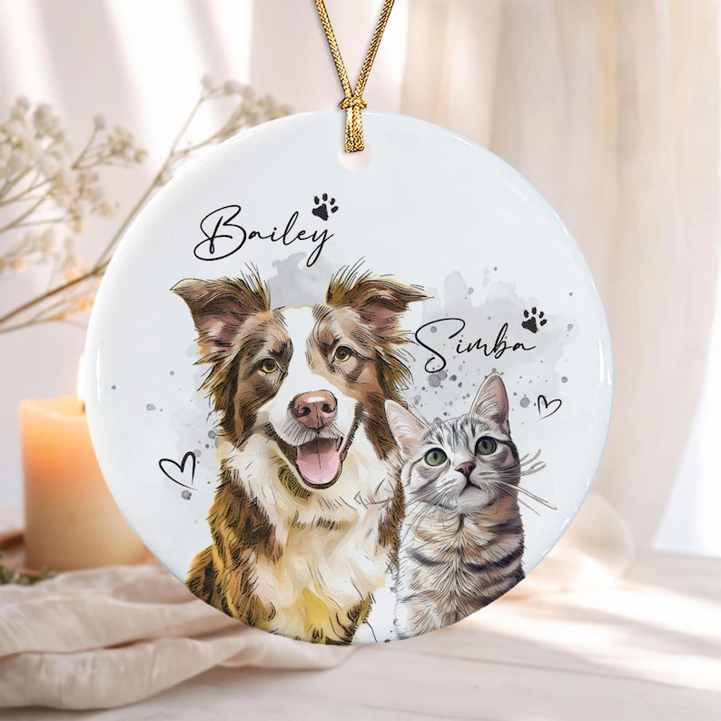 A round white ceramic ornament featuring a watercolor-style illustration of a brown and white dog and a gray tabby cat.