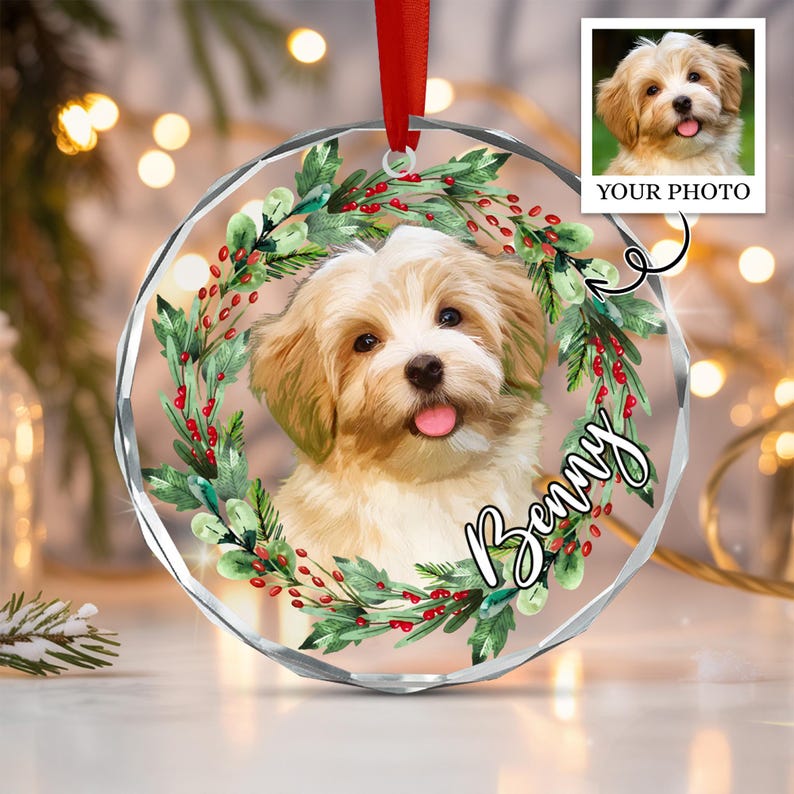 A circular clear acrylic ornament featuring a portrait of a light-colored puppy with a pink tongue, framed by a wreath of green leaves and red berries.