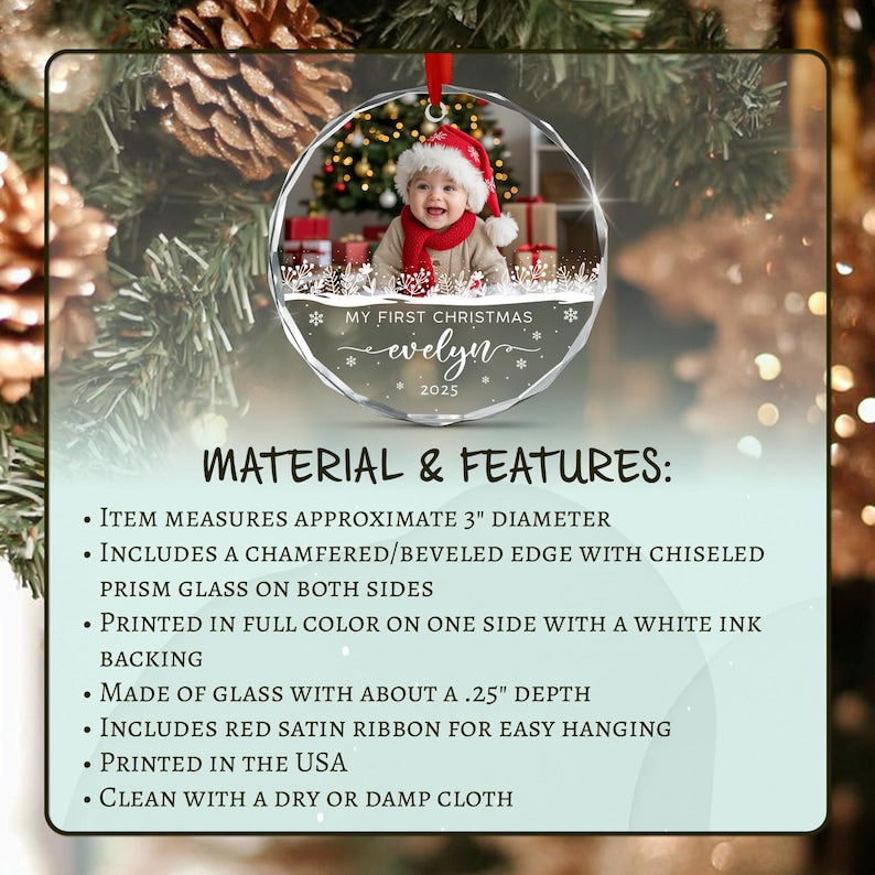 A round glass Christmas ornament with a beveled edge and red satin ribbon. The ornament features a photo of a baby in a Santa hat and red scarf, with the text MY FIRST CHRISTMAS evelyn 2025.