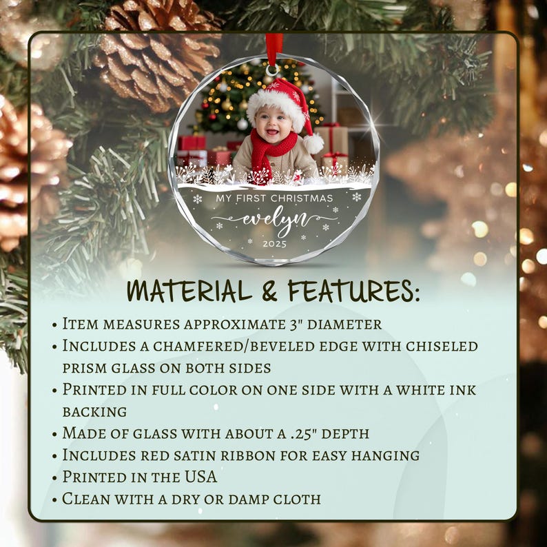 A round glass Christmas ornament with a beveled edge and red satin ribbon. The ornament features a photo of a baby in a Santa hat and red scarf, with the text MY FIRST CHRISTMAS evelyn 2025.