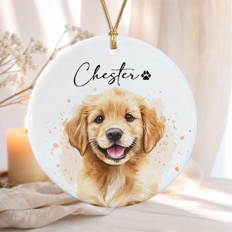 A round white ceramic ornament featuring a watercolor-style illustration of a golden retriever puppy. The name Chester is printed in black script above the puppy, accompanied by a small black paw print icon.