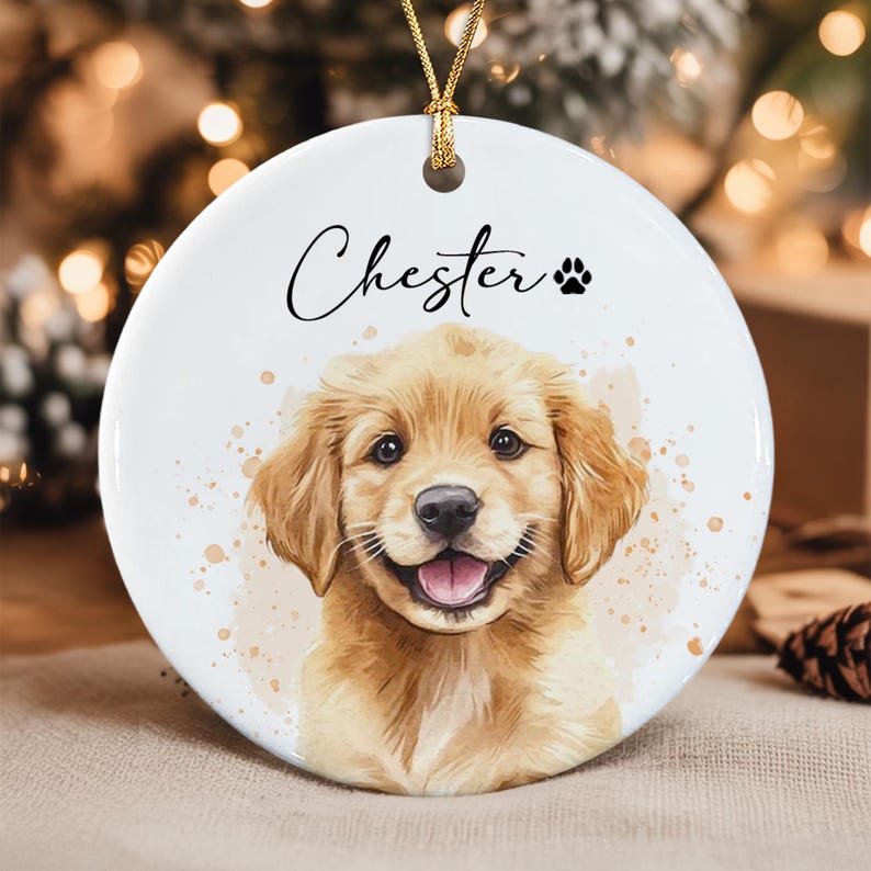 A round white ceramic ornament featuring a watercolor-style illustration of a golden retriever puppy with a smiling expression.