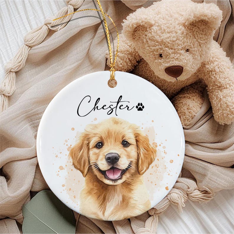 A round white ceramic ornament featuring a watercolor-style illustration of a golden retriever puppy.