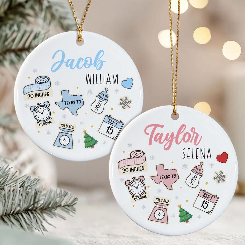 Two round white ceramic ornaments with gold hanging strings. One features the name Jacob William in blue, the other Taylor Selena in pink.