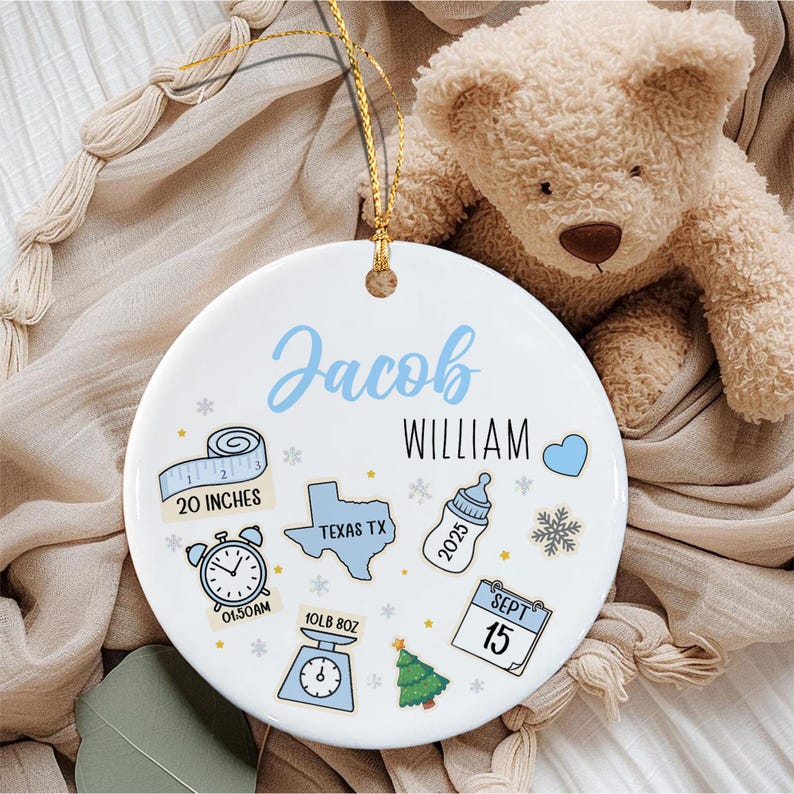 A round white ceramic ornament with a gold hanging string featuring the name Jacob William in blue and black text.