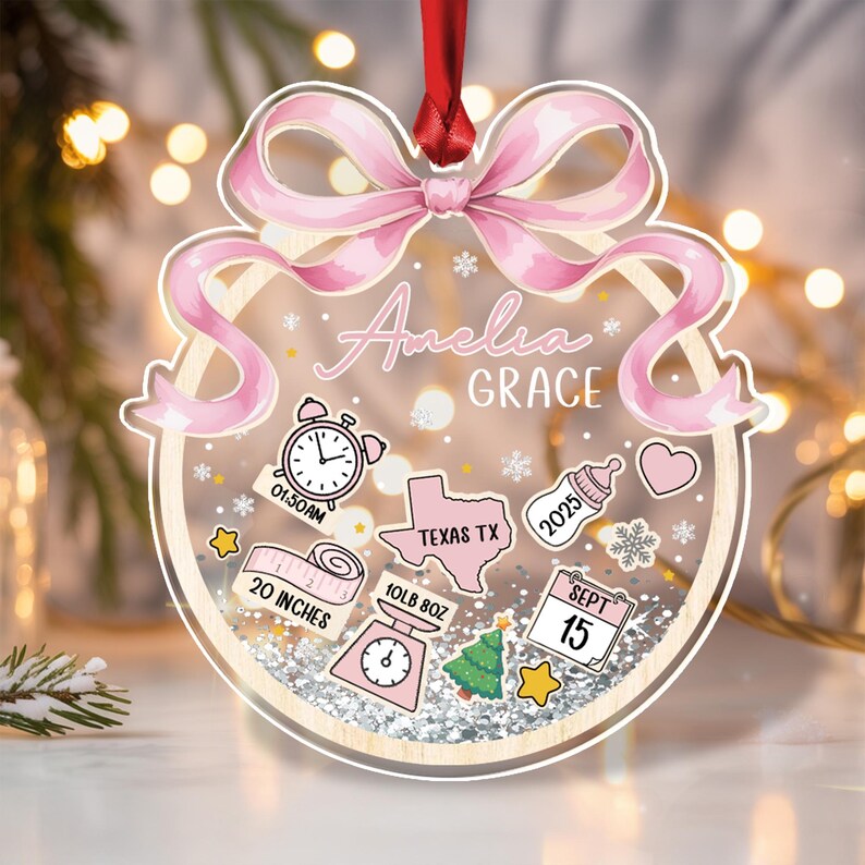 A personalized baby ornament with a pink bow and the name "Amelia Grace." The ornament includes illustrations of a clock, Texas, a baby bottle, and a measuring tape.