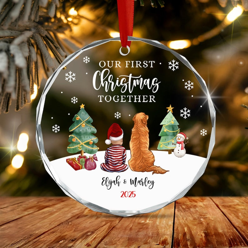 A round, clear acrylic Christmas ornament featuring the text "OUR FIRST CHRISTMAS TOGETHER" above an illustration of a child in red and white pajamas and a golden dog sitting in snow.