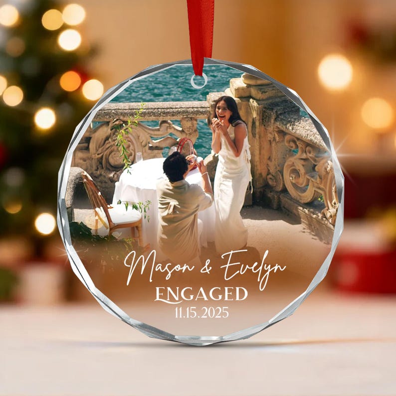 A circular faceted glass ornament featuring a printed photograph of a couple during a proposal. The text reads Mason & Evelyn ENGAGED 11.15.2025.