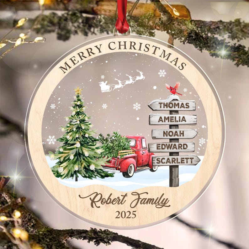 A round wooden Christmas ornament featuring a red truck carrying a green tree, a signpost with the names Thomas, Amelia, Noah, Edward, and Scarlett, a red cardinal, Santa's sleigh, the text Merry Christmas, Robert Family.