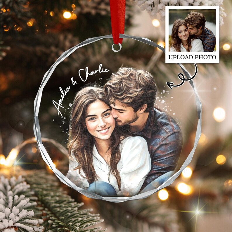 A circular clear acrylic ornament featuring a printed illustration of a couple embracing, with the names Amelia & Charlie written in white script.