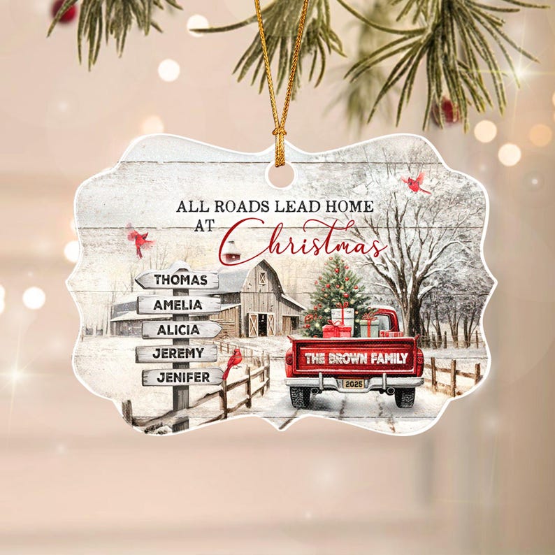 A decorative ornament with a scalloped edge featuring a winter scene with a red pickup truck, a barn, and a signpost listing the names Thomas, Amelia, Alicia, Jeremy, and Jenifer. The text reads All Roads Lead Home At Christmas.
