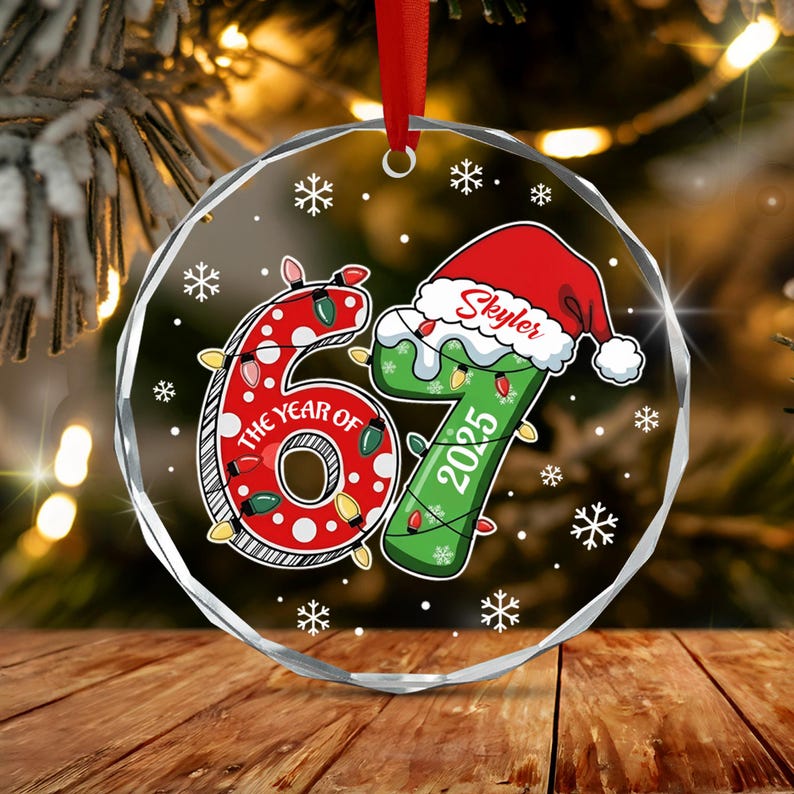 A round, clear acrylic Christmas ornament featuring the number 67 in red and green. The red 6 is decorated with white polka dots and string lights.