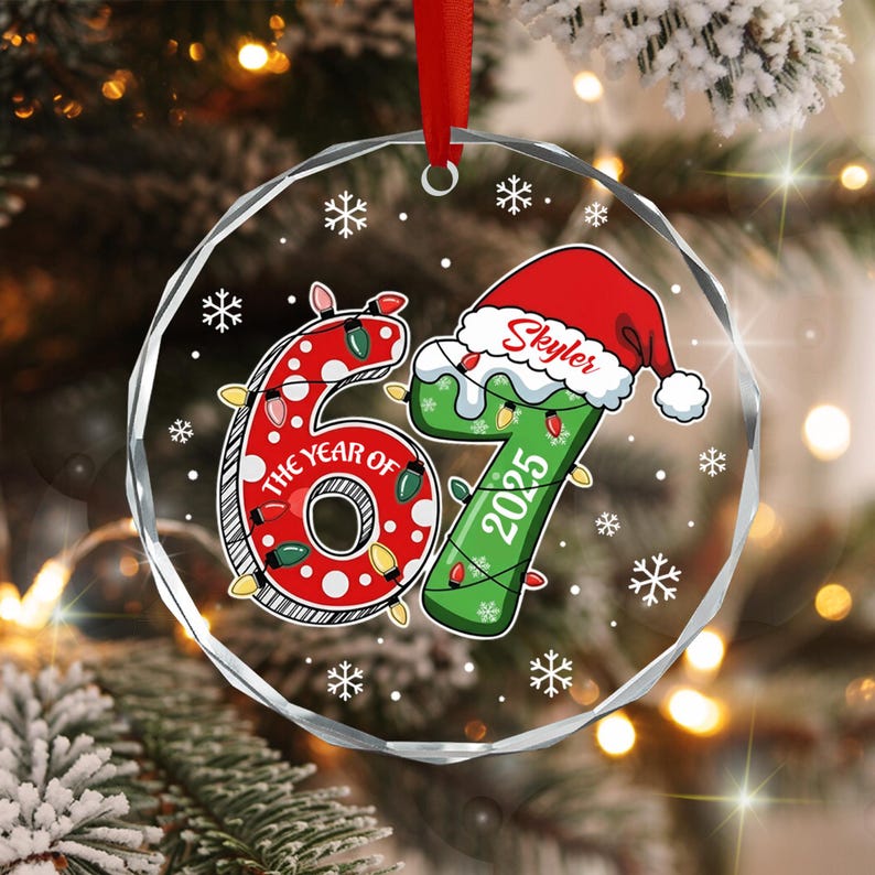 A circular clear glass ornament with a red ribbon hanger featuring the number 67. The red number 6 is decorated with white polka dots and string lights.