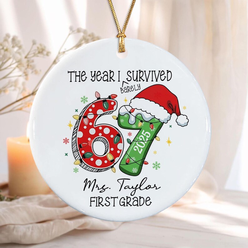 A round white ceramic ornament featuring the text THE YEAR I BARELY SURVIVED 67, with a red polka-dot 6 and a green 7 wearing a Santa hat. The number 7 includes the year 2025. Below is the text Mrs.